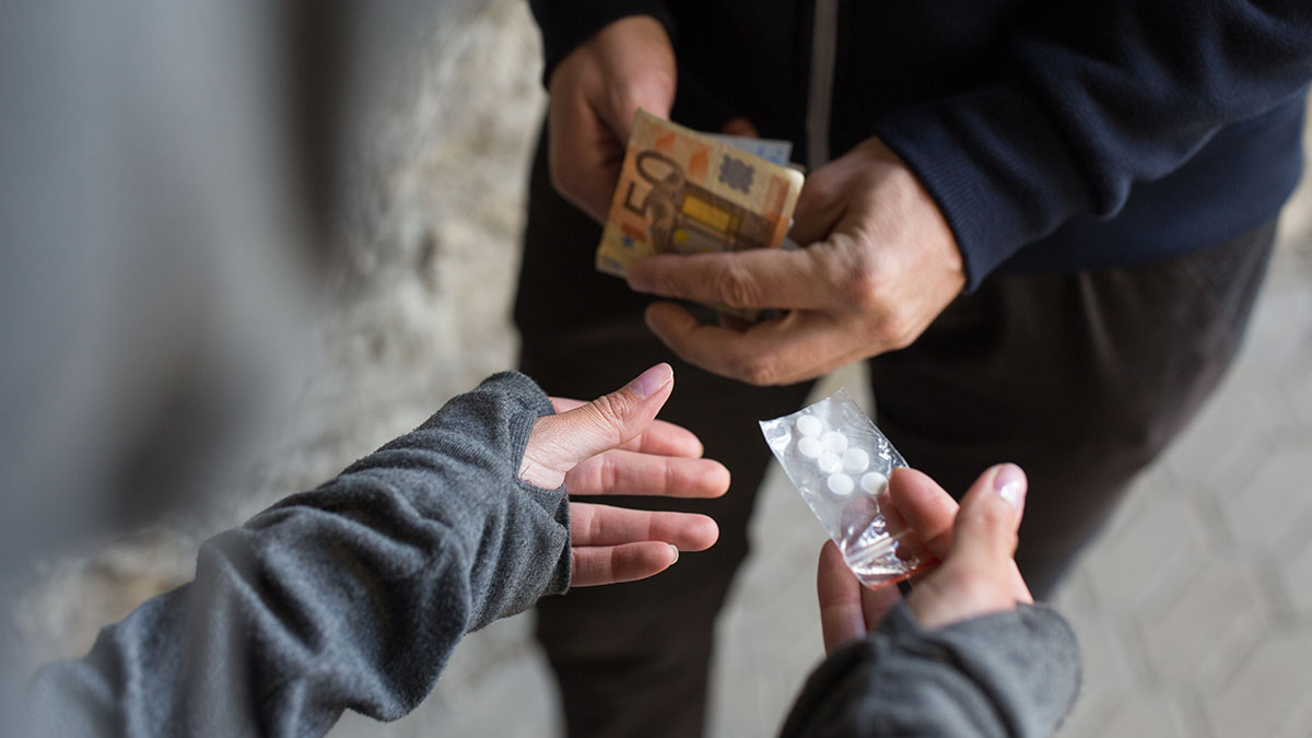 Image of a street drug deal. Graphic explains factors which contribute to drug addiction.