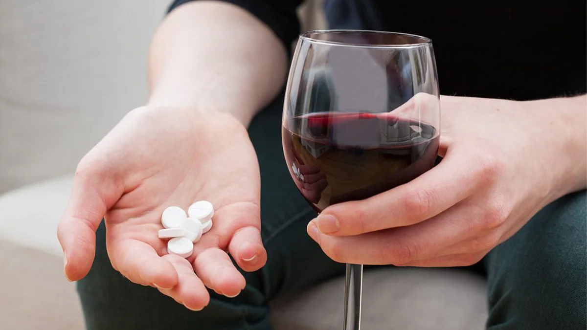 Person holding wine in one hand and pills in the other. Combining alcohol with your prescription can negatively affect mental health.