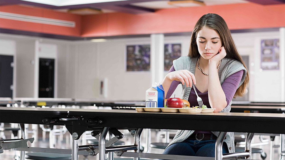 Teenage girl sitting in the school cafeteria, not eating her lunch. Anxiety and anorexia have a close relationship, often fueling each other