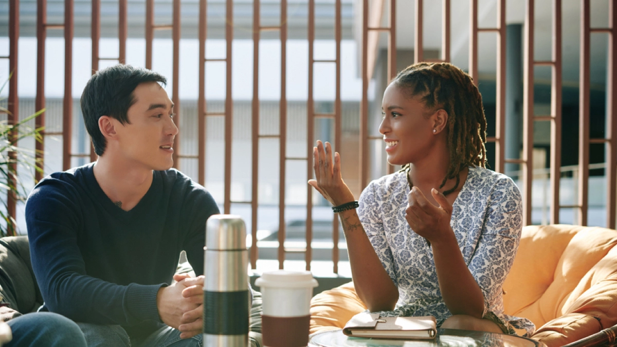 Woman speaking to man over coffee. She approaches him with empathy, as you should when confronting someone about their addiction.