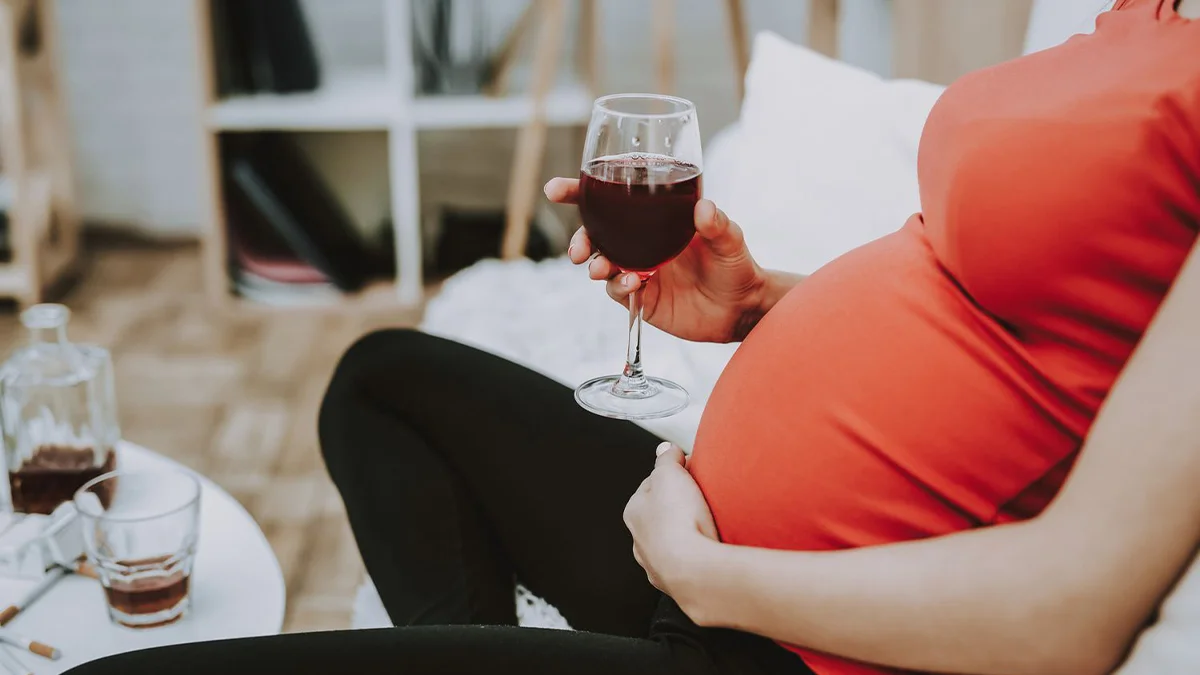 Pregnant woman holding a glass of red wine. Text explains any substance ingested by the mother can potentially reach the fetus.