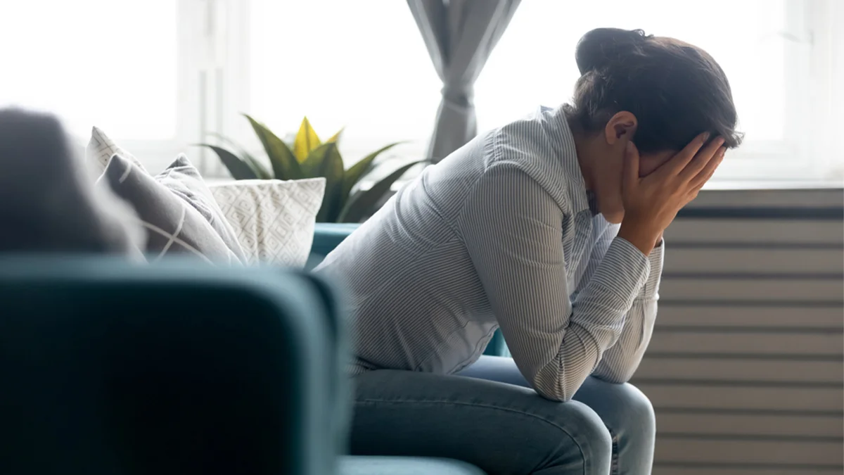 Profile of a woman sitting on a couch with her head in her hands. Mental health and addiction are intricately intertwined.