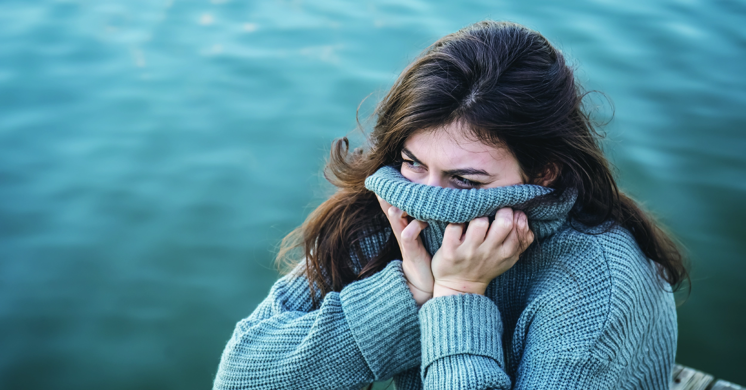 Woman sitting with her turtleneck pulled over her face. White text on a red background explains SAD’s effects on mental health.