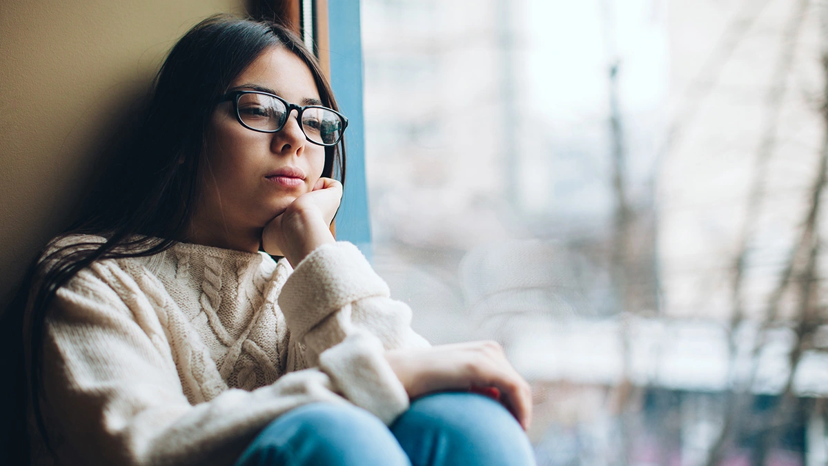 Young woman sitting and gazing out the window. Seasonal Affective Disorder is a form of depression which recurs seasonally.