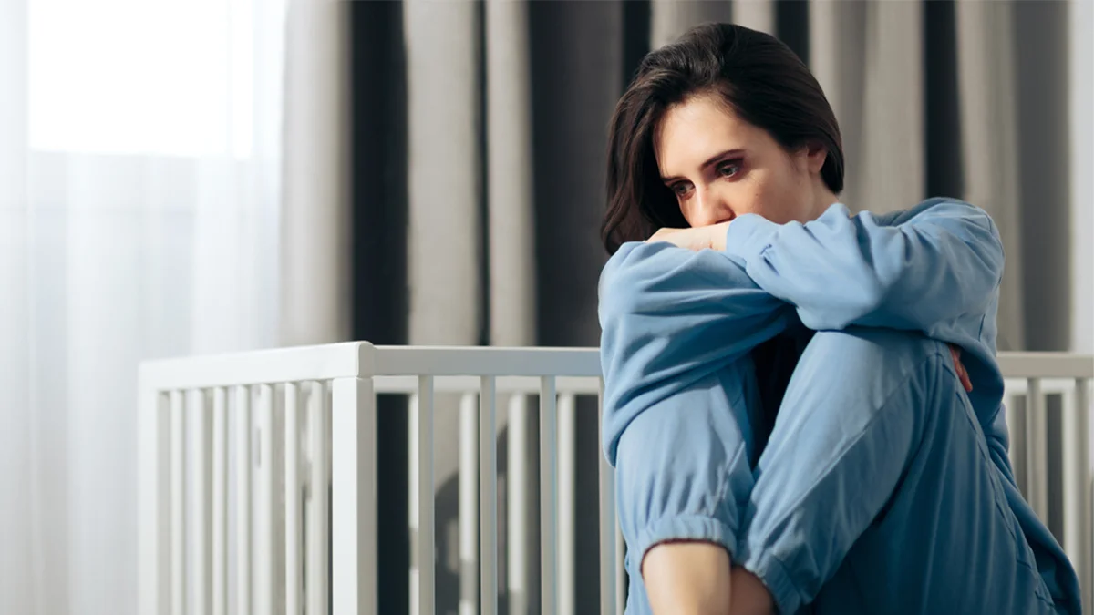 Woman sitting on the floor in front of a crib.