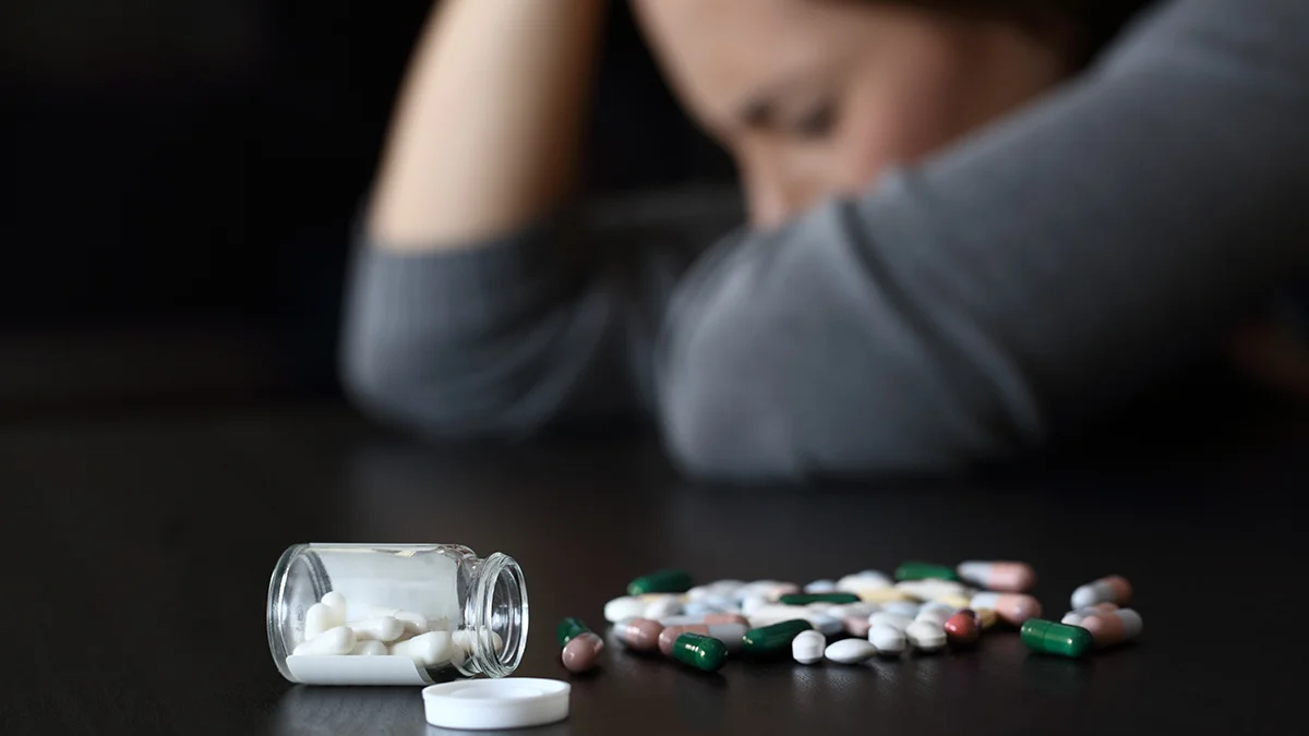 A variety of pills spilled on table with woman in the background
