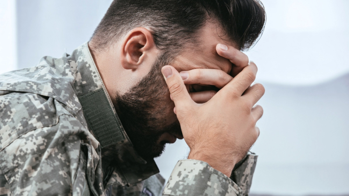 Man in army fatigues holding his face in his hands.